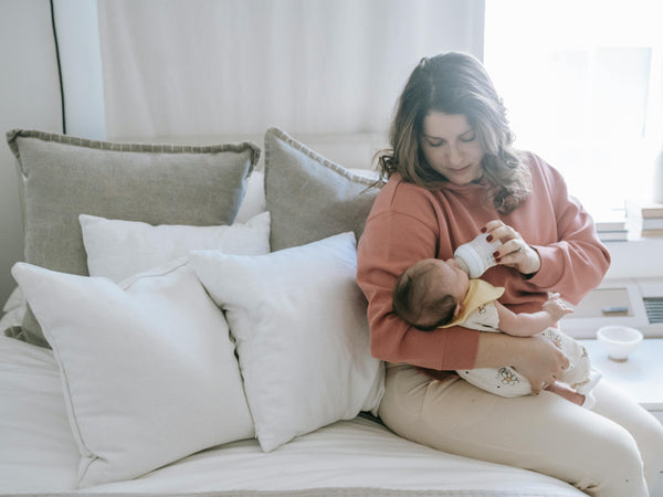 Mother holding her newborn baby in a quiet dimly lit room during the early postpartum fourth trimester