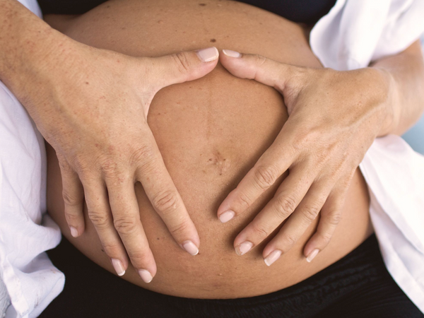 Close-up of a pregnant woman's bump with hands resting gently on skin in soft natural light