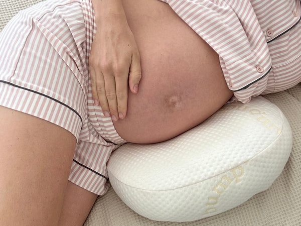 Pregnant woman resting comfortably on her side in bed with soft neutral bedding