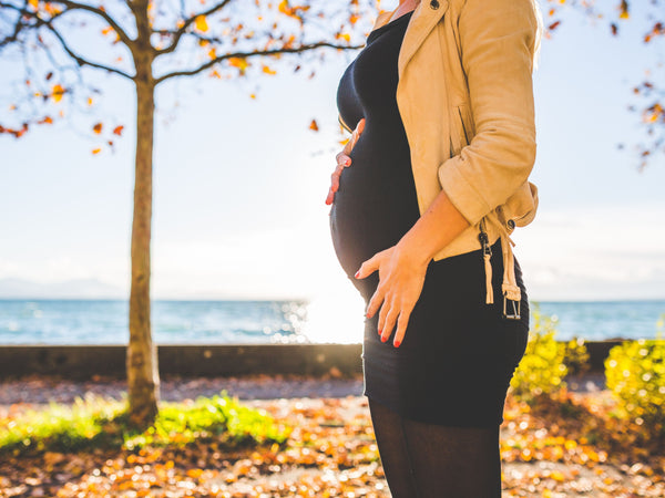 Pregnant woman standing outdoors in soft morning sunlight during pregnancy