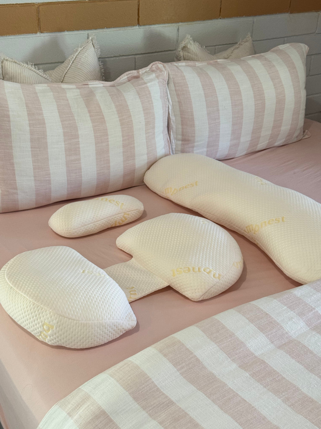 A well-organised bedroom with a pregnancy pillow sleep setup on a bed with neutral bedding in soft natural light