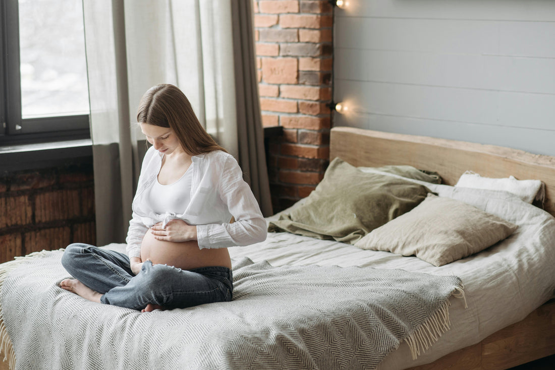 Pregnant woman sitting quietly by a window in soft natural light looking calm and reflective