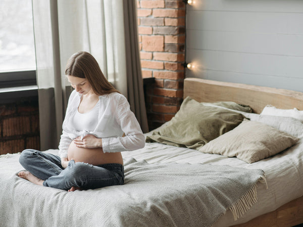 Pregnant woman sitting quietly by a window in soft natural light looking calm and reflective