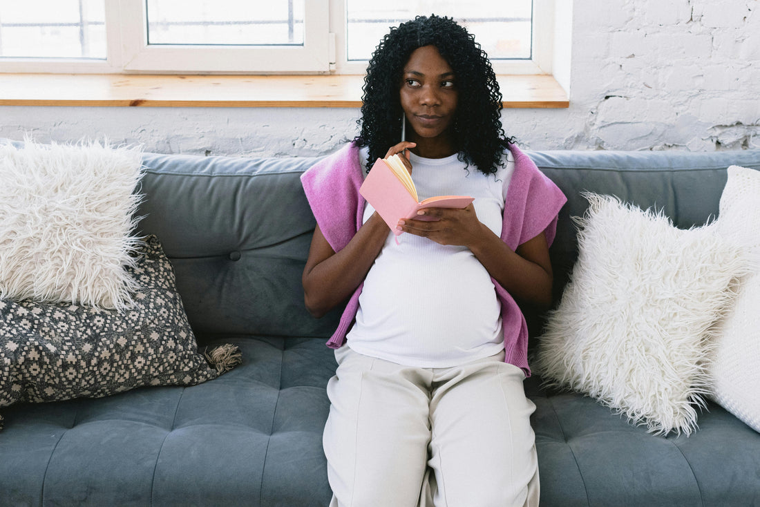 Pregnant woman sitting at a table writing her birth plan at home in soft natural light
