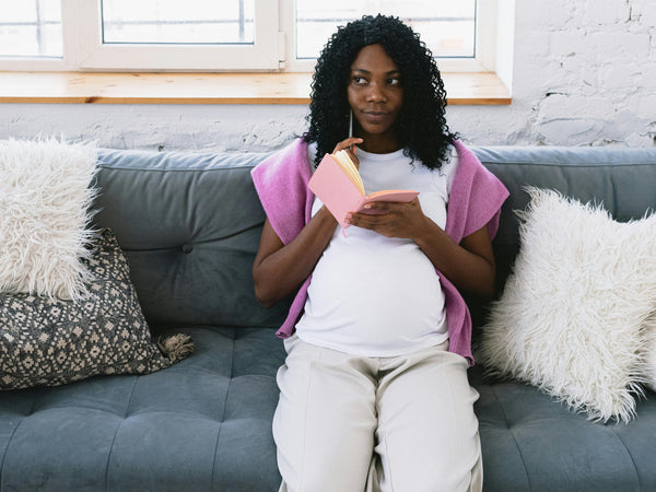 Pregnant woman sitting at a table writing her birth plan at home in soft natural light