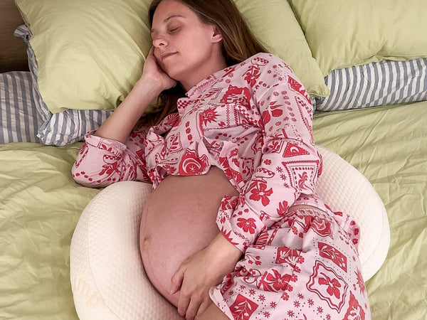 A compact pregnancy pillow setup with small components on a neatly made bed with neutral bedding in natural light