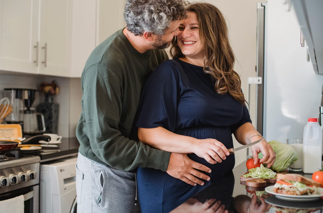 Woman sitting at a kitchen table with plain food and water during first trimester nausea in soft natural light