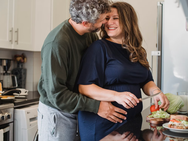 Woman sitting at a kitchen table with plain food and water during first trimester nausea in soft natural light
