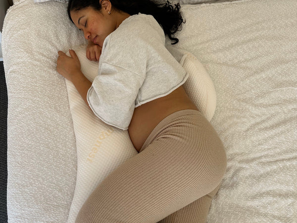 Pregnant woman lying comfortably on her side in bed with pregnancy pillow providing back pain support
