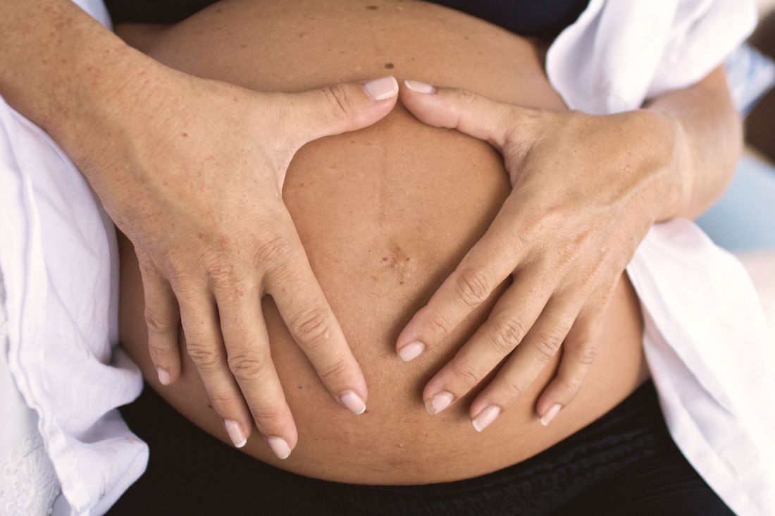 Close-up of a pregnant woman's bump with hands resting gently on skin in soft natural light