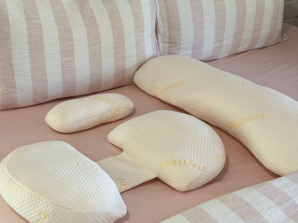 A pregnancy pillow on a neatly made bed with neutral bedding in soft natural light
