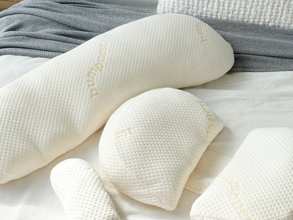 A maternity pillow arranged on a neatly made bed with neutral bedding in soft natural light